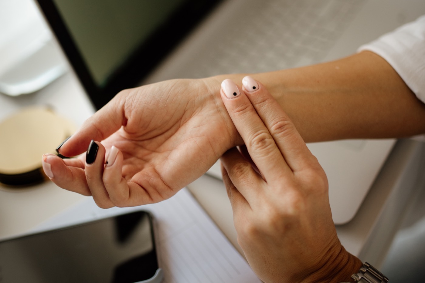 A person at a desk pressing two fingers to the inside of their wrist to feel their pulse