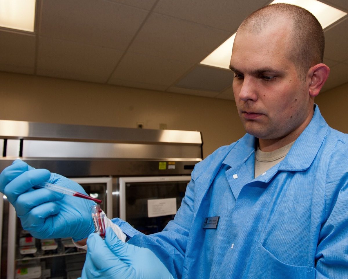 A laboratory technician in gloves draws blood from a collection tube with a pipette