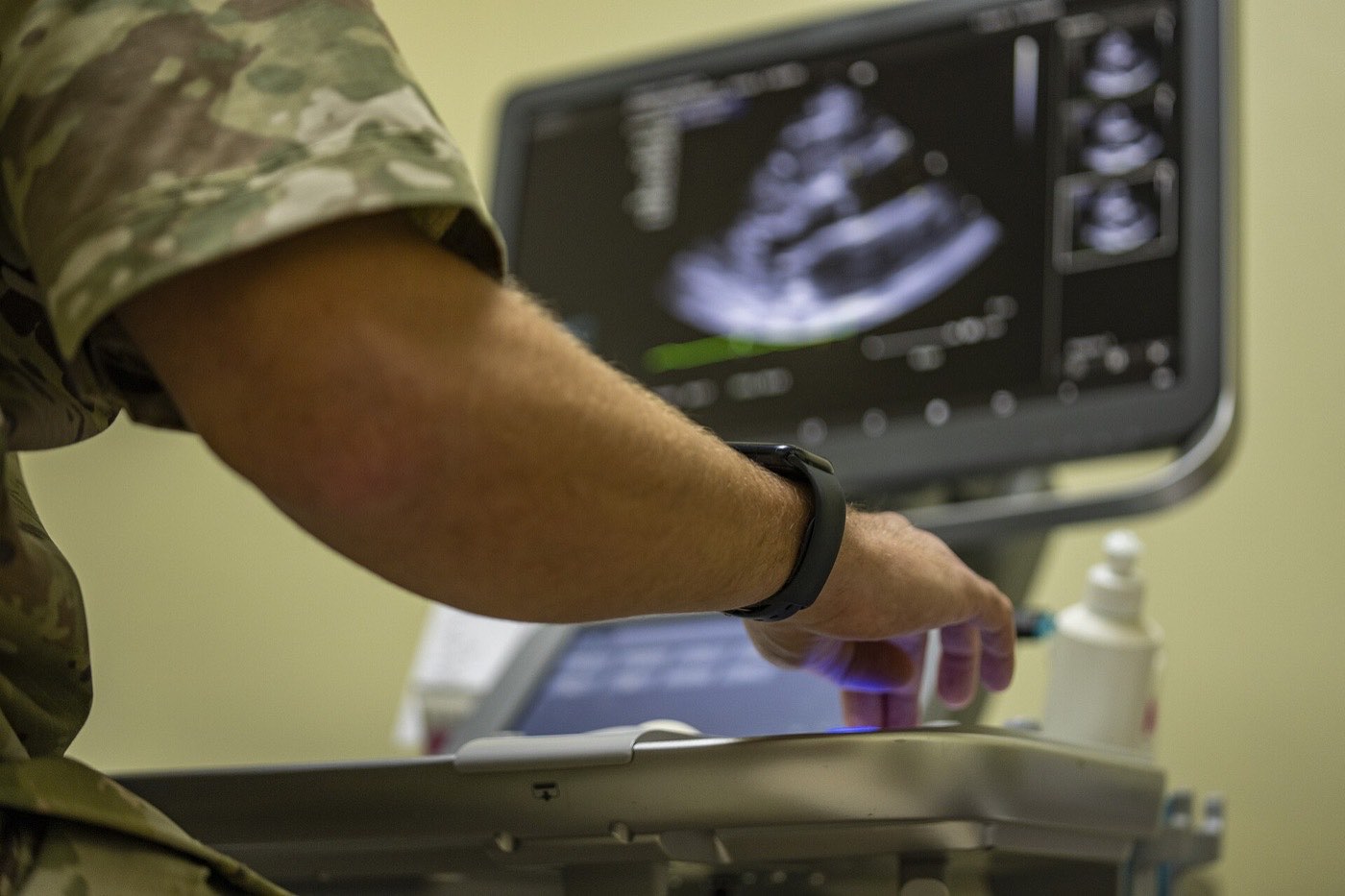 A clinician adjusts the controls of an ultrasound machine displaying a moving image of the heart